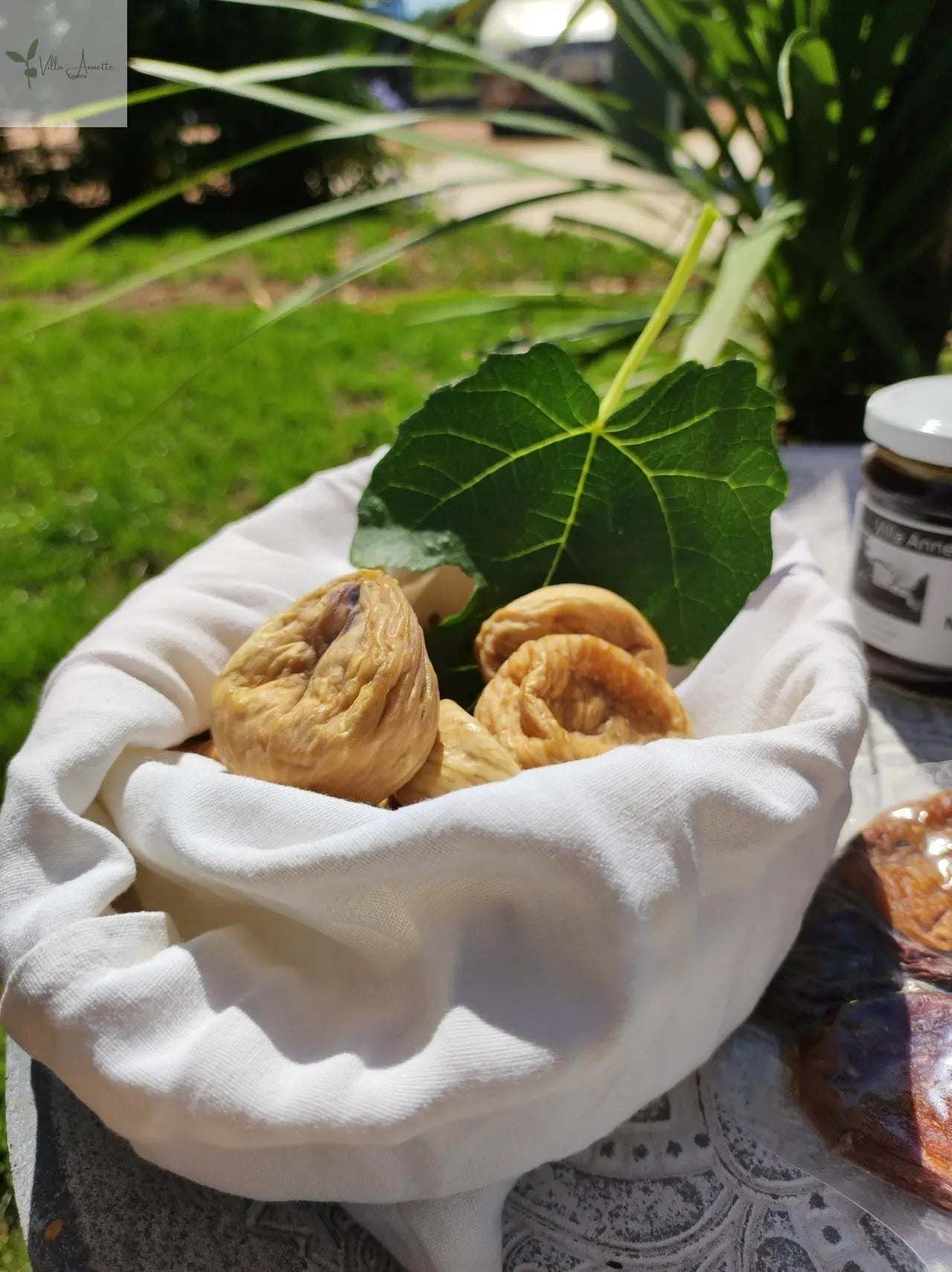 Dried figs in a white cloth with green leaves in sunlight.